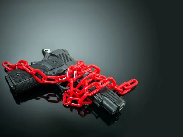Концепция управления оружием. Красная цепь вокруг пистолета на черном зеркале с прожектором блеск пистолета — стоковое фото