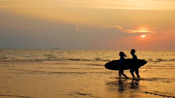Silhouet van jonge gelukkige mensen, Surf man en meisje rennen met lange surfplanken bij Sunset Tropical Beach. Surfer op het strand in de kust bij zonsondergang tijd met mooi licht. watersport activiteit — Stockfoto