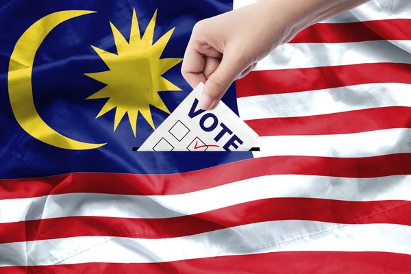 Malaysia general election concept. close up hand of a person casting a ballot at elections during voting on canvas Malaysia flag background.