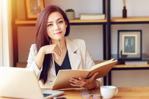 Dizüstü bilgisayar ve kitap ile çalışan güzel ve kendine güvenen Asyalı iş kadını portresi işyerinde iş yönetmek, kamera bakmak ve gülümseme. mutlu iş kadını kavramı — Stok fotoğraf