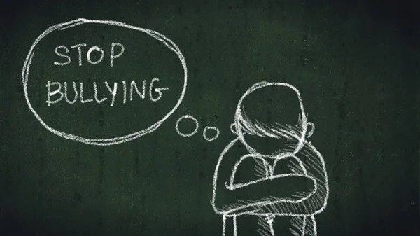 Sad young boy sitting on the floor with text stop bullying written with chalk on chalkboard. social problems of humanity — Stock Photo, Image