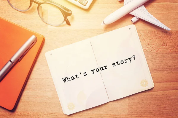 what's your story? notebook with text at blank page on wooden background with glasses and plane model