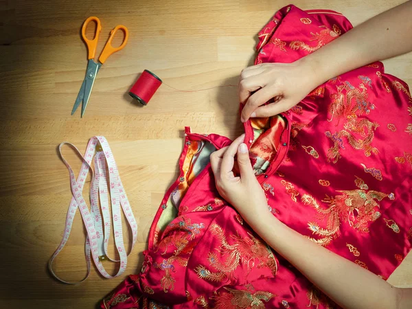 Vista superior das mãos femininas cortadas costura vestido Cheongsam com agulha no local de trabalho de costureira com equipamento de costura — Fotografia de Stock