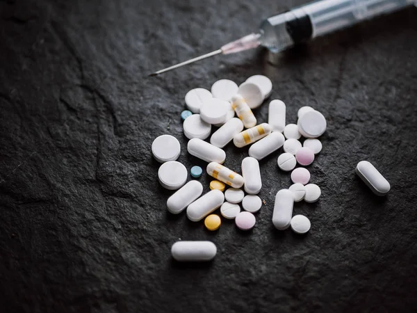 Blandade färgglada farmaceutiska medicin piller tabletter och kapslar med Hypodermic spruta injektion nål på svart sten bakgrund. apotek och läkemedel för behandlingskoncept — Stockfoto