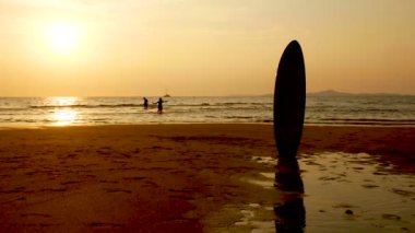 4k. gün batımında sahilde çalışan ve suda oynayan kız ve erkek kardeşi siluet. güzellik ve neşeli genç arkadaşlar eğlenmek, yaz gün batımı nda püskürtme.