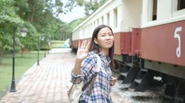 4k. Asyalı turist kadın tren istasyonunda giden trende el sallayarak. Hoşça kal