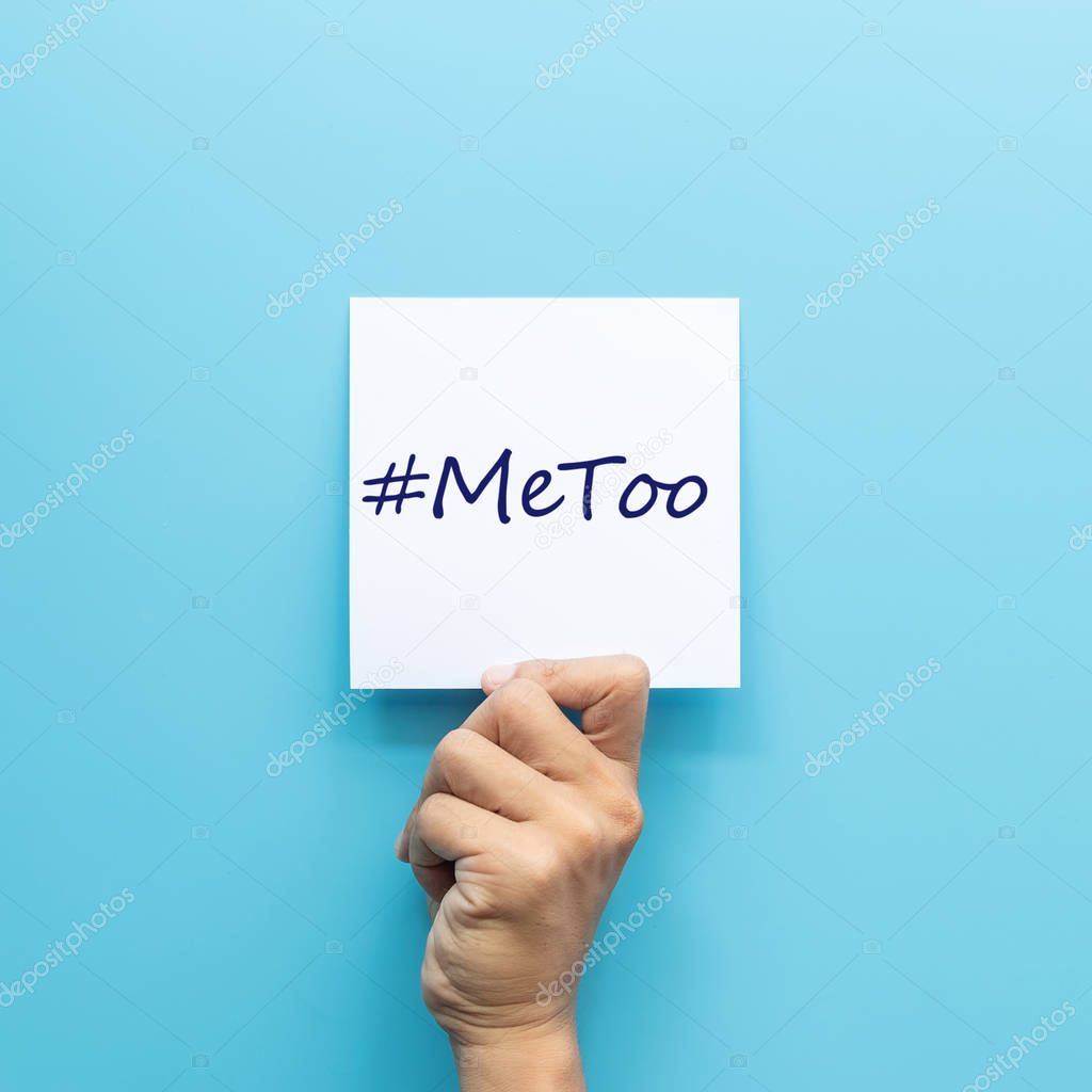 hashtag #MeToo on white paper in hand isolated on blue background. #MeToo is a campaign for movement against sexual harassment and sexual assault.