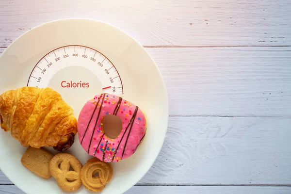 Concepto de conteo de calorías y control de alimentos. rosquilla, croissant y galletas en plato blanco con escamas en la lengua para medir calorías — Foto de Stock