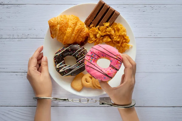 Kalori kontrolü, gıda diyet ve kilo kaybı kavramı. iki elin üst görünümü, el kelepçeleri ile kontrol edildi, ahşap masada beyaz çanak gelen donut tutarak — Stok fotoğraf