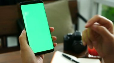 4k görüntü. yakın kadın el kahve dükkanında yeşil ekran ile akıllı telefon tutan, telefon ekranında parmak dokunuşu kullanarak