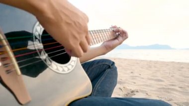 4k. gün batımı nda plajda akustik gitar çalan bir adamın yakın çekim, dinlenmek hissi