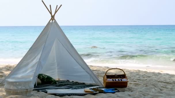 浪漫的白色野餐帐篷 白色沙滩上有篮子食物 背景是清澈的海水和蓝天 包括海洋的声音 — 图库视频影像