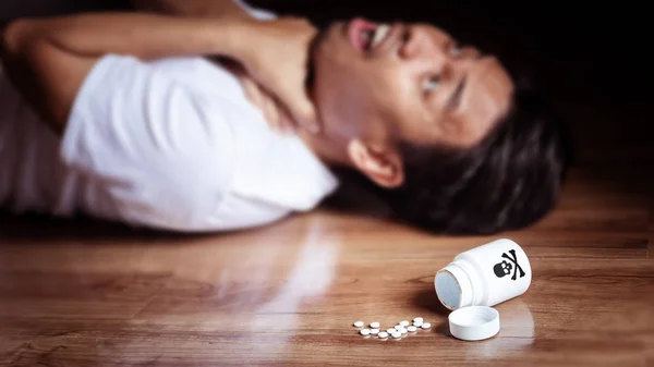 Άνθρωπος να ξαπλώσει στο πάτωμα του δωματίου με συμπτώματα βασανιστηρίων από την κατανάλωση δηλητηρίου για αυτοκτονία, λευκό μπουκάλι με το λογότυπο σταυρό κρανίο πέφτει στο πάτωμα. προβλήματα κατάθλιψης, ψυχικών και στρες ασθενών — Φωτογραφία Αρχείου