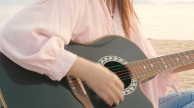 4k. gün batımı sırasında hafif rüzgar ile plajda akustik gitar çalan uzun saçlı kadın yakın, rahatlık hissi