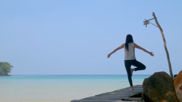 暑假期间 一名妇女在海边的木桥上练习瑜伽时 单腿站立 有吸引力的年轻亚洲妇女站在瑜伽姿势 — 图库视频影像