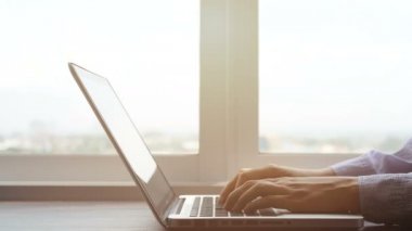 4k. dizüstü bilgisayar klavyesi, pan kamera üzerinde yazarak eller. yüksek binadan pencere görünümü ile çalışma alanında dizüstü bilgisayar üzerinde çalışan iş kadını, sabah ışığı.