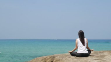 4k. meditasyon yoga yapan bir kadın yaz tatili sırasında deniz üzerinde ahşap köprü üzerinde poz. çekici genç Asyalı kadın lotus veya sukhasna meditasyon poz oturur