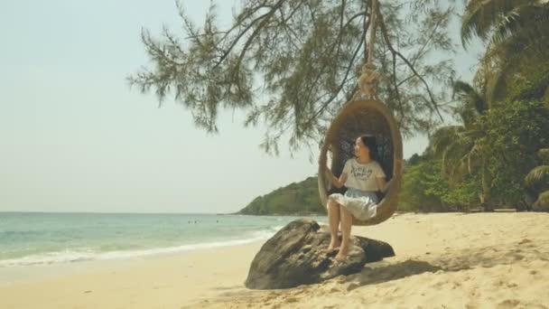 女人感到放松 在暑假假期的闲暇时间在沙滩上的树下打秋千 — 图库视频影像