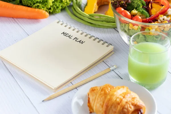 Calories control, meal plan, food diet and weight loss concept. meal plan writing on notebook planner with salad, fruit juice, bread and vegetable on dining table
