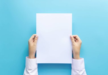 El afiş veya davetiye mavi arka planda izole kadar boş beyaz boş mektup kağıt boyutu A4 tutan ellerini yakın.