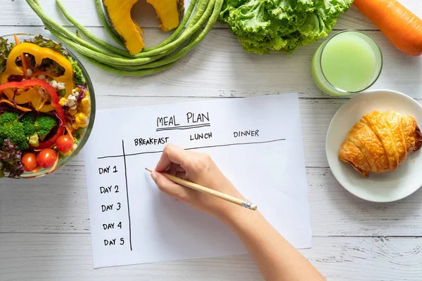 Kalorikontroll, måltidsplan, kost och viktminskning koncept. ovanifrån av hand fyllning måltid plan på veckobord med sallad och färska grönsaker på matbordet — Stockfoto