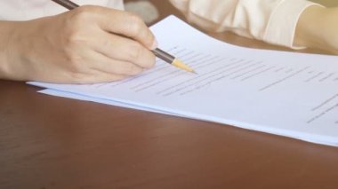 4 bin. Kadın kağıt üzerinde okuyor, sayfayı çeviriyor ve belgedeki metni işaretlemek için kalem kullanıyor