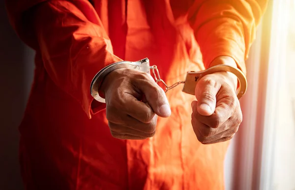 close up of prisoner\'s hands with handcuffs in orange jumpsuit at prison
