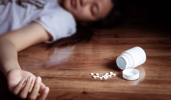 Överdoseringskoncept. närbild av piller och kvinna som tar medicin överdos liggande på golvet med öppna piller flaska — Stockfoto