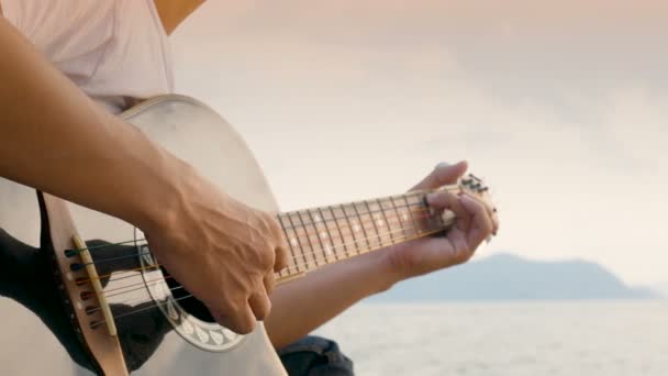 日没時にビーチでアコースティックギターを弾く男のクローズアップ リラックス感 — ストック動画