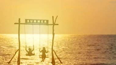 4k. mutlu çift siluet gün batımı sırasında deniz üzerinde salıncak ile sallanan zevk, üstüne yaz işareti. mutlu yaz tatili konsepti