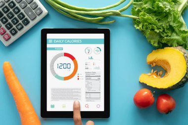 Kalori sayma, diyet, gıda kontrolü ve kilo kaybı kavramı. taze sebze ve hesap makinesi ile yemek masasında tablet üzerinde Kalori sayacı uygulaması kullanan kadın