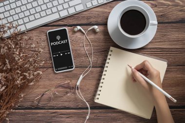 Podcast ses içeriği konsepti. Mobil akıllı telefon ekranında, kahve fincanı, kulaklık, gözlük, defter ve kalemle birlikte cep telefonu ekranında podcast uygulaması. yayın medyası