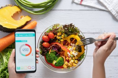 Kalori sayımı, diyet, gıda kontrolü ve kilo kaybı konsepti. Yemek masasındaki akıllı telefon ekranında salata, meyve suyu, ekmek ve taze sebzeyle kalori sayacı uygulaması. sağlıklı beslenme