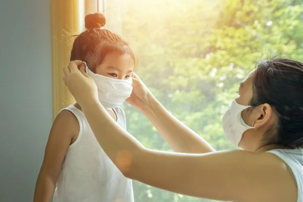 Asian family with children in face mask, mother prepare to put face mask on her kid before leaving house to go school for prevent germs during the coronavirus or covid-19 outbreak. new normal concept