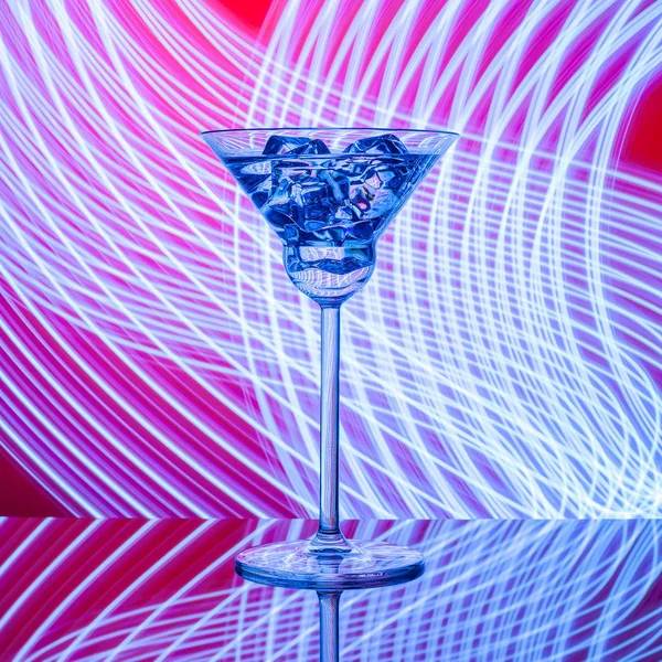 Glass with cocktail on the glass table on the neon lights background