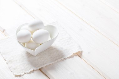 Beyaz ahşap arka planda bir kasede beyaz yumurtalar