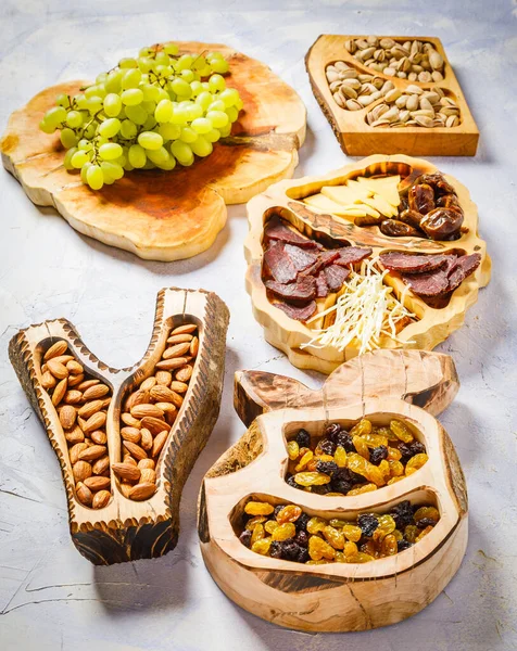 Assortment of nuts, walnuts, pistachios, almonds, meat, cheese, raisins and grapes on wooden boards
