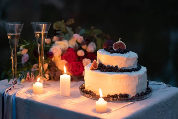 結婚式の装飾 メガネ キャンドルと結婚式の花束と夜のテーブルの上にブルーベリーとイチジクの装飾と白い釉薬のケーキ — ストック写真