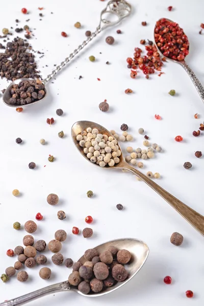 black, red, white pepper peas in metal spoons on a white background. chili, paprika