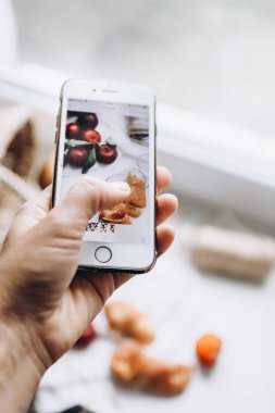 Bir el bir akıllı telefon tutar ve sulu erik ve kruvasan bir natürmort resmi alır