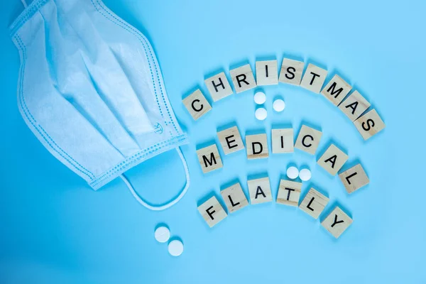Wooden letters with the inscription christmas medical flatly, blue medical mask on a blue background. Concept christmas and new year 2020