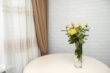 Beyaz duvarın üzerinde duran vazodaki sarı güller. Metnin için Yer