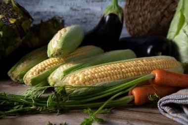 Yeşil başlıklı taze havuç, ahşap bir masada mısır ve patlıcan.