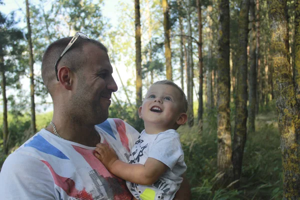 Fars dag glad pappa håller sin lille son i famnen i en tallskog. Familjesemestrar och umgås — Stockfoto