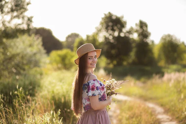 bir saman şapka ince bir kız ve çayır papatyalar bir buket tutan bir saman çanta ile. Yaz günbatımı, mutluluk kavramı, huzur, yaşam aşkı