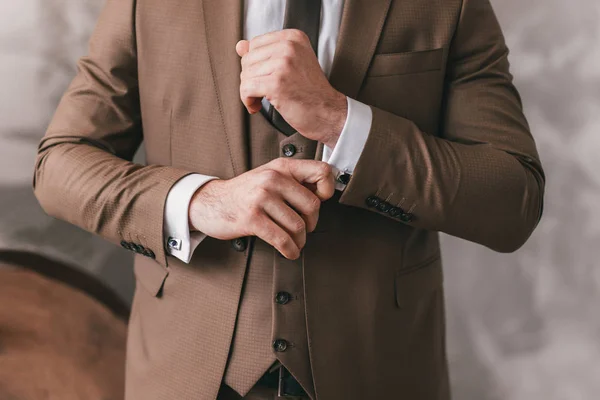 Zarif genç moda adam onları sabitleme sırasında onun kol düğmeleri bakıyor. Erkek ellerinin fotoğrafı. Yakışıklı damat kahverengi resmi takım elbise, beyaz gömlek ve kravat giymiş düğün için hazırlanıyor