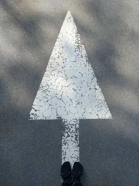 Large white arrow symbol drawn on asphalt road