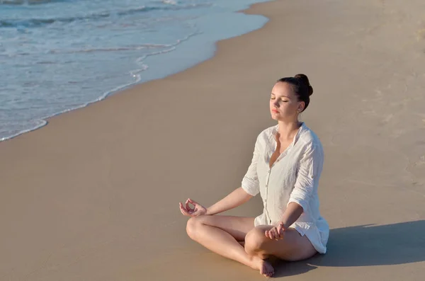 Junge Frau meditiert am Strand am Meer. — Stockfoto