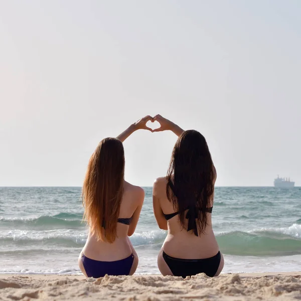 Duas meninas na praia segurando as mãos umas das outras para formar uma forma de coração — Fotografia de Stock