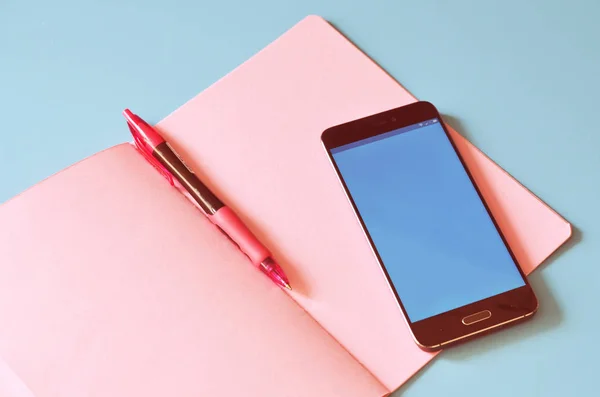 Mavi masa üstünde smartphone ve pembe defter. Tasarım için alay